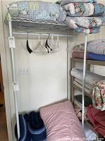 Metal clothing rack with comforters folded on its top shelf and some comforters rolled on the floor beneath it
