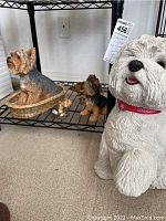 Photo showing a large white dog figurine with tongue out and red collar, along with smaller dog figurines on a lower metal shelf including Yorkshires and hedgehogs.