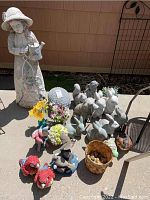 Photo showing all garden statues and figurines including large girl statue, multiple rabbits, bird figurines, and other decorations grouped on pavement