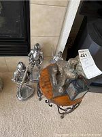 Overall view of three metal knight figurines and dog statue on wooden display table with wrought iron base.