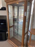Front and side view of the oak-tone wood framed display cabinet with five clear glass shelves and front glass door.