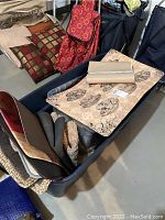 Tote tub filled with various mats and small rugs featuring different colors and patterns in a basement setting