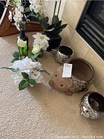 Photo showing several hedgehog-shaped planters and faux flower arrangements including white roses, tulips, and orchids placed on carpeted floor by a fireplace.
