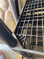 Close-up image of a black plastic storage shelf corner showing the grid shelf and a supporting post.