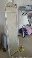 Full view of one panel of the cream wicker room divider leaning against a wall next to the brass floor lamp with white shade.