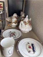 Overview of tea set pieces including teapot, cups, sugar bowl, cream pitcher, and decorative plates on shelf.