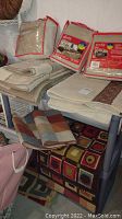 Multiple small rugs and packaged bed protector and chair slipcover on shelving