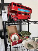 Photo showing the red double decker bus model on top shelf and three Spode holiday plates below, one in original box.