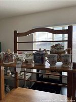 Wide view showing the collection of porcelain teapots, cups, and containers on a wooden shelf with window light