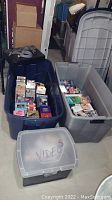 Photo showing over 50 VHS tapes in two large blue and grey plastic storage bins plus one smaller transparent bin labeled 'video',' category: video tapes
