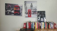 Wall art and related items displayed on and above a shelf filled with books, mainly London-themed prints and plaques highlighted with red accents