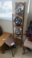 View of the small wooden 4-tier shelf with three fans placed on shelves, not included in the lot, and the small wooden side table positioned nearby.