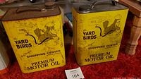 Photo showing two vintage yellow metal oil cans with Yard Birds mascot and text, placed on a red carpet.