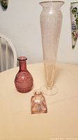 Three pink glass vases on a table: one tall bubble glass vase, one smaller patterned vase, and one very small charm vase.