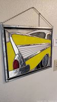 Full view of rectangular stained glass depicting rear of a yellow 1957 Chevrolet with metal frame and hanging chain.