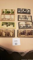 Eight stereoscope cards laid out in two columns on a table, with visible variations in card colors and photographic content showing historical and domestic scenes.