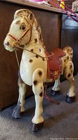 Front left angle view of the antique ride-on horse showing full body, saddled seat, reins and spots with wear marks.