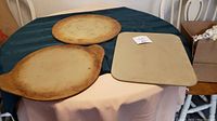 Three Pampered Chef baking stones displayed on a table with two round stones and one square stone.