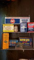 Full view of vintage automotive advertising metal sign and assorted vintage auto parts boxes arranged on a metal wall hanger