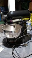 KitchenAid black tilt-head stand mixer with stainless steel mixing bowl installed and power cord laid on table