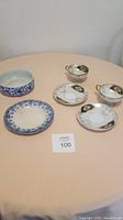 Six vintage china items on a peach tablecloth: three Royal Sealy tea cups/saucers with gold and black patterns, one Bourne & Leigh blue floral plate, and a blue and white bowl.