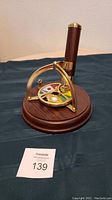 Front angled view of wooden and brass musical kaleidoscope on round wooden base showing colored disk and brass arches.