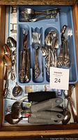 Drawer with organized Oneida silverware: dinner forks, knives, spoons, and teaspoons, all with decorative handles, laid in a blue cutlery tray. Also includes two large adaptive spoons with rubber handles outside tray.