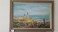 Framed oil painting of two girls walking through a flower field by the sea, with cloudy sky and birds flying.