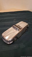View of polished aluminum vintage roadster car model showing front and side profile on dark fabric background.