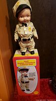 Full view of the 13 inch Shell gas station attendant doll standing atop the matching tin box showcasing full uniform and accessories.
