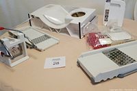 Photo showing set of kitchen slicers and graters on a beige surface including a meat slicer, French fry cutter, mandoline slicer, and grater with insert.