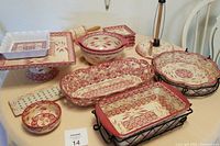 Full lot arranged on table showing multiple Temptations ceramic bakeware pieces in cranberry pattern including bread basket, bowls, plates, pedestal plate, hot plate, and bread basket with metal racks.