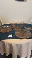 Wide view of all pink depression era glass items arranged on table including plates, creamer, sugar set, and tumbler.