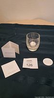 Overview of the Glassy Baby votive candle holder with original label and info cards on a dark cloth.