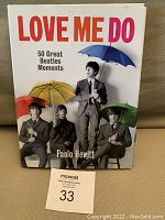Front cover of the Beatles book 'Love Me Do: 50 Great Beatles Moments' by Paolo Hewitt, showing The Beatles with colorful umbrellas and title prominently displayed.