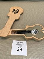 Guitar-shaped wooden box open showing the Beatles watch inside with black leather band and black and white image of Beatles on watch face.