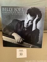 Front cover of Billy Joel Greatest Hits Volume I & II showing Billy Joel leaning on a piano in a black and white photo.