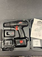 Photo showing black Jobmate cordless drill in case with battery attached, charger, and instruction manual.