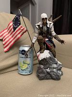 Full view of statue beside a standard can for size comparison with American Revolutionary War-era flag.