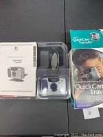 Wide view showing Logitech QuickCam Traveler camera inside clear plastic clamshell packaging with instruction manual and original box visible