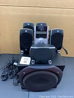 Complete speaker system with subwoofer, five satellite speakers, and control console arranged together showing the overall set.