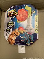 Two images of the boxed Roto-Motion Mixer Dino Lab kit showing front packaging with dinosaur models and mixer device graphic.
