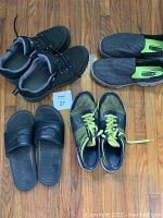Four pairs of men's shoes arranged on wooden floor: Nike slide sandals, Sketchers GoGamat slip-ons, black hiking shoes, and Reebok trainers.