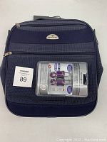 Front view of navy blue Samsonite carry on bag with visible Samsonite logo and MaxSold lot number sticker. Bag appears new and unused.