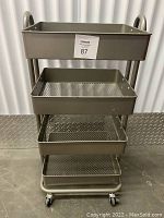 Front view of gray metal rolling cart with four rectangular shelves. Two shelves solid, two shelves mesh metal. Cart on four caster wheels, two of which have locking brakes. Sized for storage and utility use.