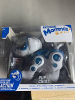 Blue and white Tekno Mommas Pup Chiot robot dog toy in sealed clear plastic packaging with multiple action features listed on the box, showing the front view of the toy and branding.