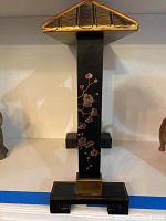 Black pillar of the gong frame with floral design in gold and red, base visible.