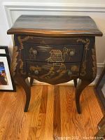 Front view of the dark wood night stand showing two drawers with painted Asian-style scenic designs including houses and trees and ornate round drawer pulls.