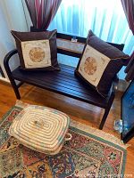 Wooden bench with two decorative pillows on the seat and large woven wicker basket with lid on the floor in front of bench