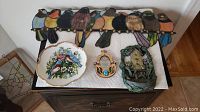 Full lot overview showing stained glass bird wall hanging, decorative bird plate, and two bird-themed plaques.